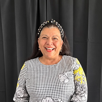 Office Manager Norma Valle Smiling In Front Of Grey Curtain