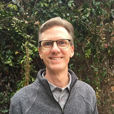Chiropractor James “Billy” Wright Smiling Outdoros In Front Of Foliage